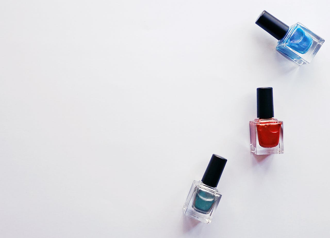 services-02 Three colorful nail polish bottles arranged creatively on a white backdrop, showcasing vibrant beauty products.