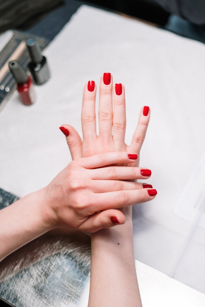 services-01 Close-up of elegant red nail polish on hands in a salon setting, showcasing modern manicure art.